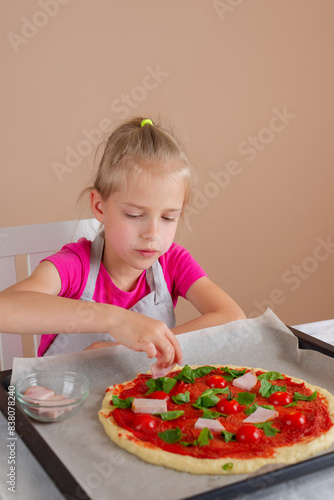 Girl puts ingredients on pizza dough. Yeast-free pizza, homemade, handmade, DIY pizza. Vertical orientation.