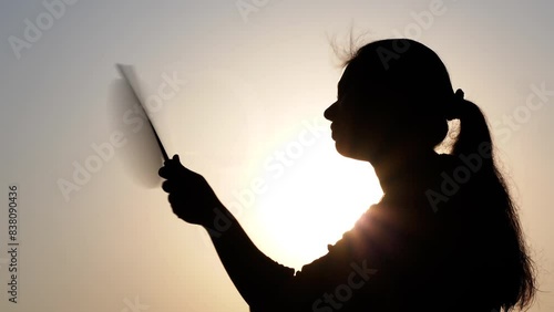 A woman sitting under the hot sun tries to cool her body using a hand fan.
