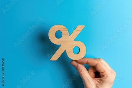 Wood percentage sign in a human hand. Blue studio background, copy space. Symbol percent. Seasonal sale, discount. Rate for finance, return. Investment ROI, credit, mortgage, tax, marketing, promotion