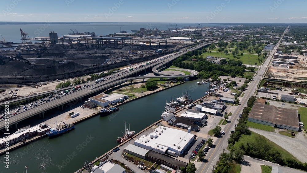 Fototapeta premium Shipyard beside interstate highway with cars traveling past coal refinery and boats in harbor 