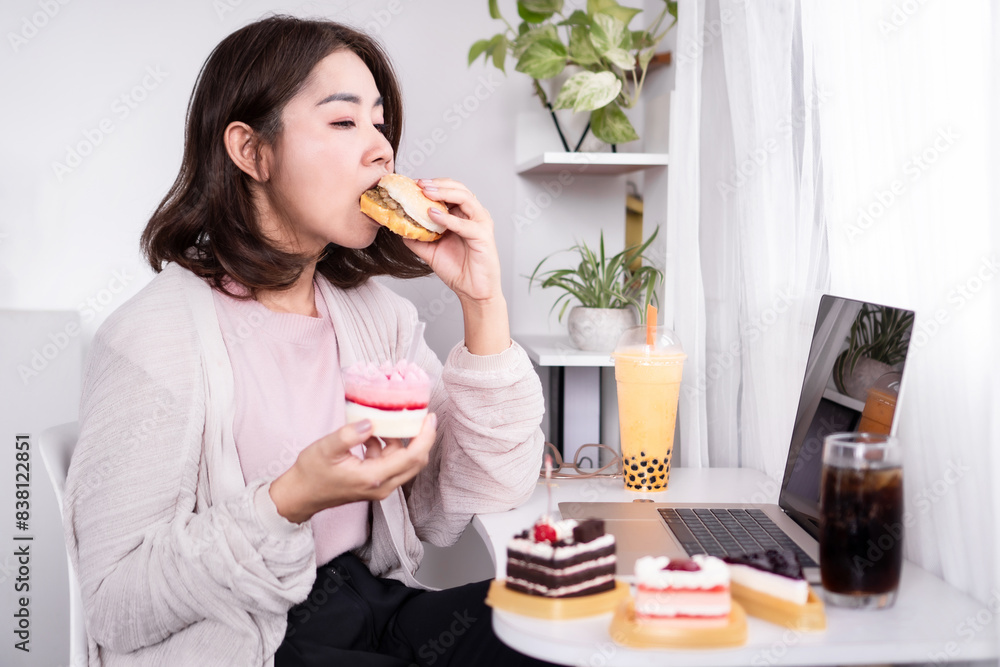 Binge eating disorder, sugar addict concept with woman eating fast food burger and desserts with some cakes , sweet drinks on table Binge eating disorder, sugar addict concept with woman eating fast food burger and desserts with some cakes , sweet drinks on table