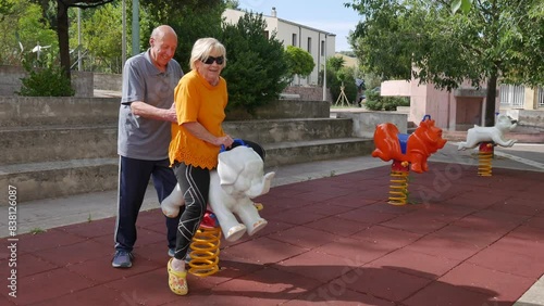 nice elderly couple playing at the children's playground, with slide, swing and rides. youth in the elderly.