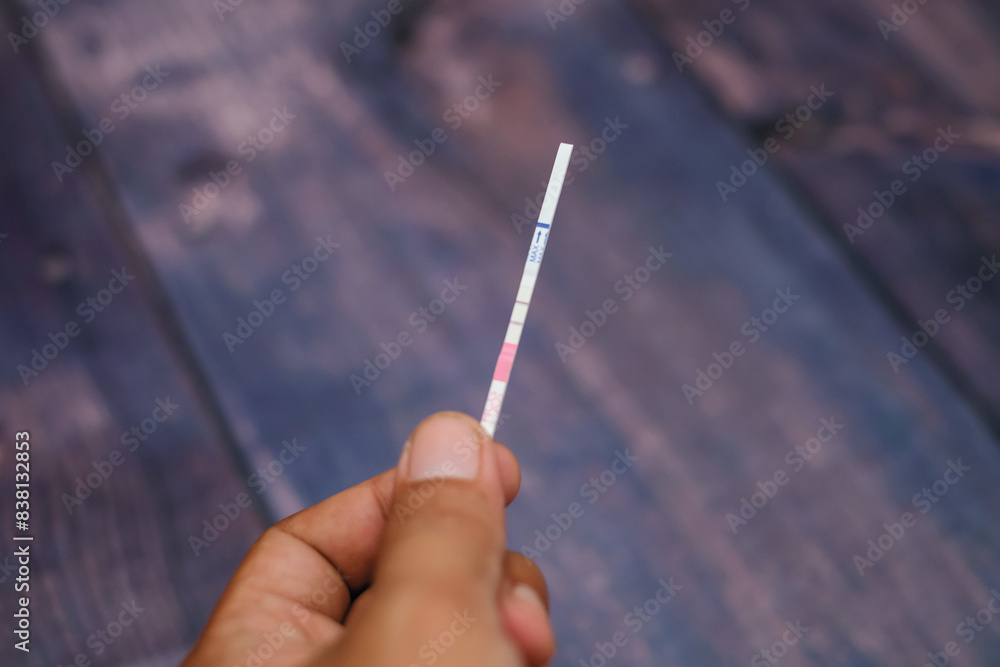 Woman hand holding positive pregnancy test strips on wood background Woman hand holding positive pregnancy test strips on wood background