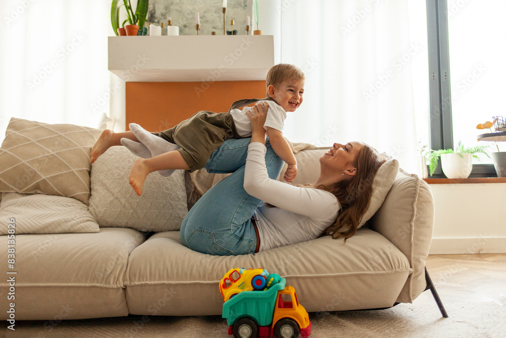 young mother holds her little son in her arms and lifts him up at home, 2-year-old boy is having fun and playing young mother holds her little son in her arms and lifts him up at home, 2-year-old boy is having fun and playing