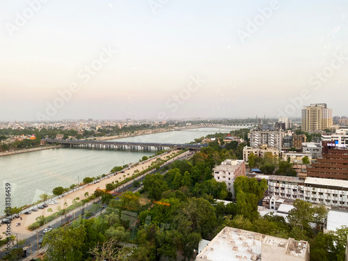 Valokuva A city view of urban Ahmedabad showcases a blend of modern buildings and lush green trees, with the serene Narmada River flowing through