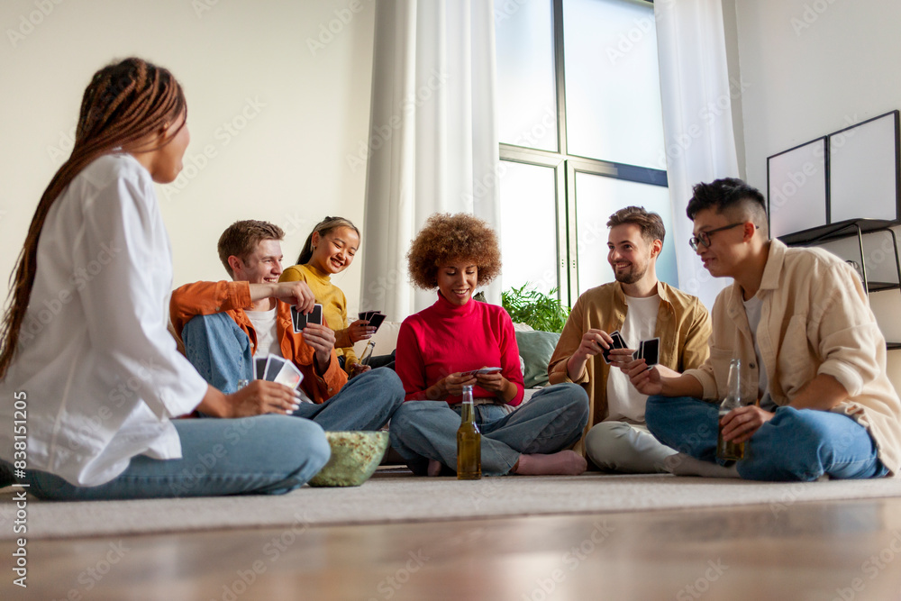 multiracial group of young friends playing cards drinking beer and having fun at home, students sitting on the floor multiracial group of young friends playing cards drinking beer and having fun at home, students sitting on the floor