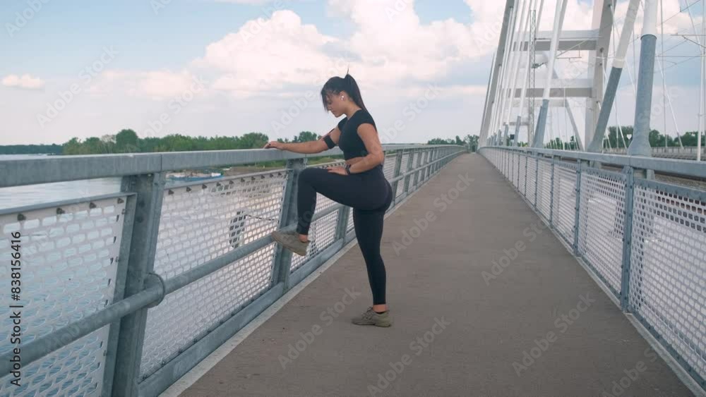 Young fitness woman in black sport outfit preparing for a run stretching her muscles at bridge. Young fitness woman in black sport outfit preparing for a run stretching her muscles at bridge.