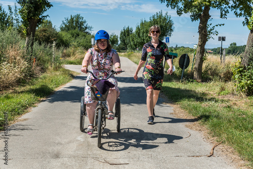 Young woman with Down syndrome on a tricycle and her friend in a dress driving through the fields at the Belgian countryside photo