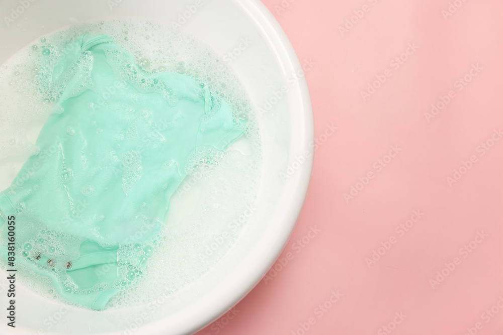 Baby clothes in washing basin on pink background, top view. Space for text Baby clothes in washing basin on pink background, top view. Space for text