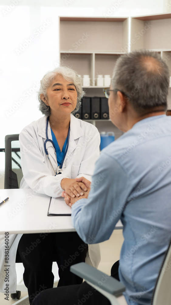 Asian female doctor and patient talking about something while sitting at the table, female doctor wearing white uniform and a stethoscope is checking the condition of an elderly male patient. Asian female doctor and patient talking about something while sitting at the table, female doctor wearing white uniform and a stethoscope is checking the condition of an elderly male patient.