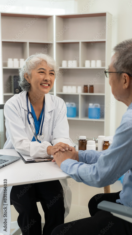 Fototapeta premium Asian female doctor and patient talking about something while sitting at the table, female doctor wearing white uniform and a stethoscope is checking the condition of an elderly male patient.
