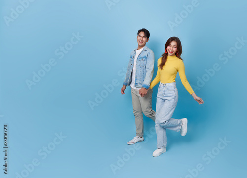 Full body smiling cheerful young Asian teen couple holding hands and walking together isolated on blue copy space studio background.