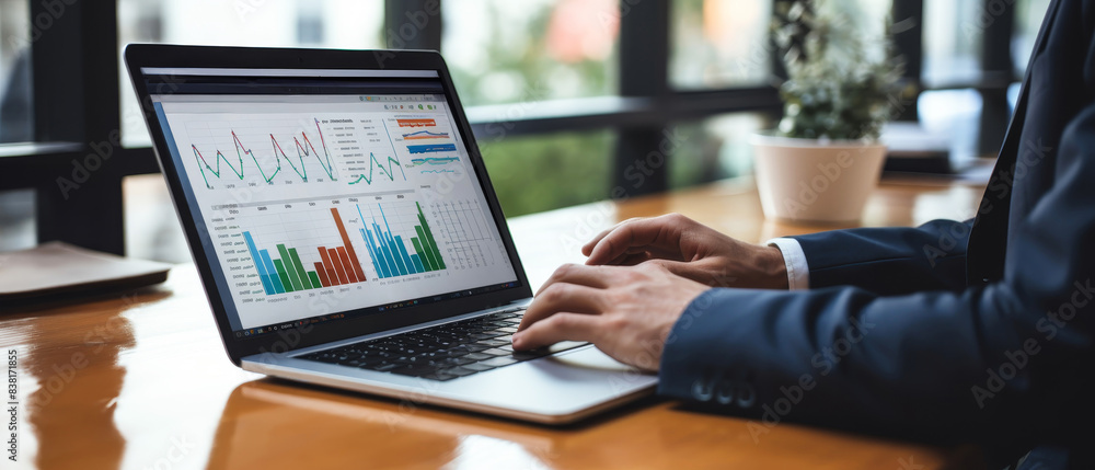 Business person working on laptop with data analytics charts. Office workspace with graphs and statistics on screen, enhancing productivity.