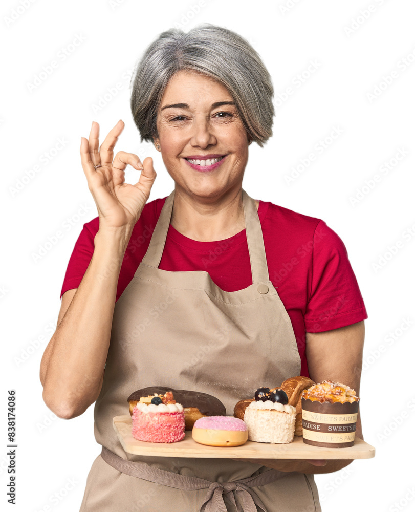 Caucasian mid-age baker with pastry tray cheerful and confident showing ok gesture.