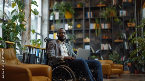 A confident businessman in a wheelchair works on his laptop in a modern, stylish office, The bright, spacious environment exudes professionalism and inclusivity