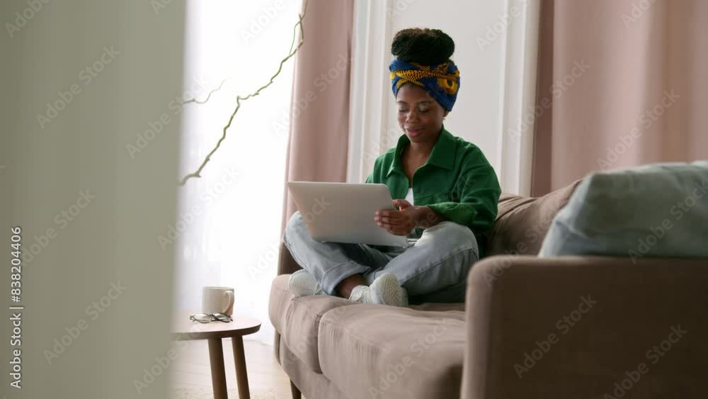 Young black woman freelancer with braids sitting on couch in living room at home, working remotely on laptop, typing on keyboard, smiling. African American female pleased student at online education. Young black woman freelancer with braids sitting on couch in living room at home, working remotely on laptop, typing on keyboard, smiling. African American female pleased student at online education.