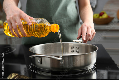 Vegetable fats. Woman pouring oil into frying pan on stove in kitchen, closeup