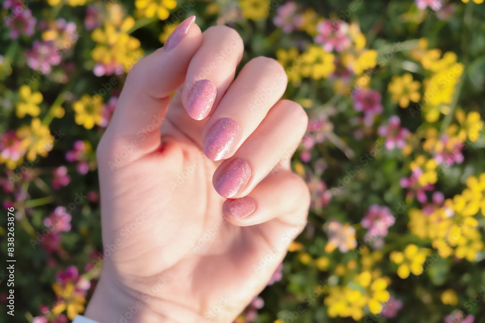Hand with Pink Glitter Nail Polish and Floral Background. Close-up of a hand with pink glitter nail polish against a background of colorful flowers. Hand with Pink Glitter Nail Polish and Floral Background. Close-up of a hand with pink glitter nail polish against a background of colorful flowers.