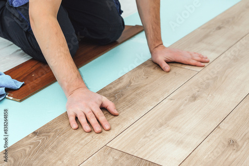 Man laying laminate flooring - closeup on male hands. Worker hands installing timber laminate floor. Easy and quick installation of the flooring. © volurol