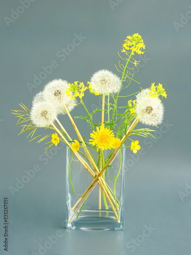 Still life with yellow wildflowers and white dandelions in a glass vase on a gray background. Japanese art of flower arrangement. Ikebana arrangement.