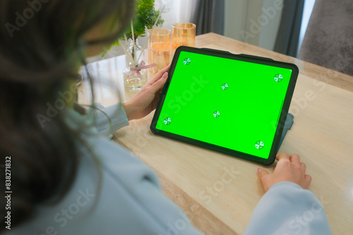 A woman uses a mobile phone or tablet with a green screen to watch videos, surf social media, or have an online conference.