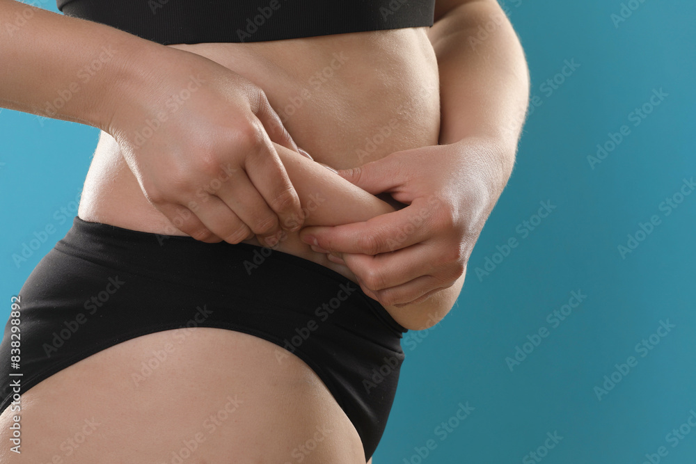 Fototapeta premium Woman touching belly fat on light blue background, closeup. Overweight problem