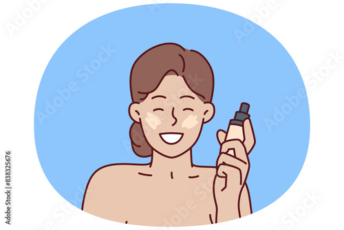 Woman with liquid foundation smiles as she puts on makeup to hide skin imperfections. Positive girl demonstrates new foundation recommending use of high-quality cosmetics for skin care
