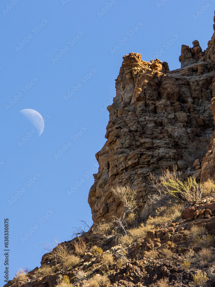 A rugged cliff in the Fish River Canyon of Namibia with the waxing moon in the background A rugged cliff in the Fish River Canyon of Namibia with the waxing moon in the background