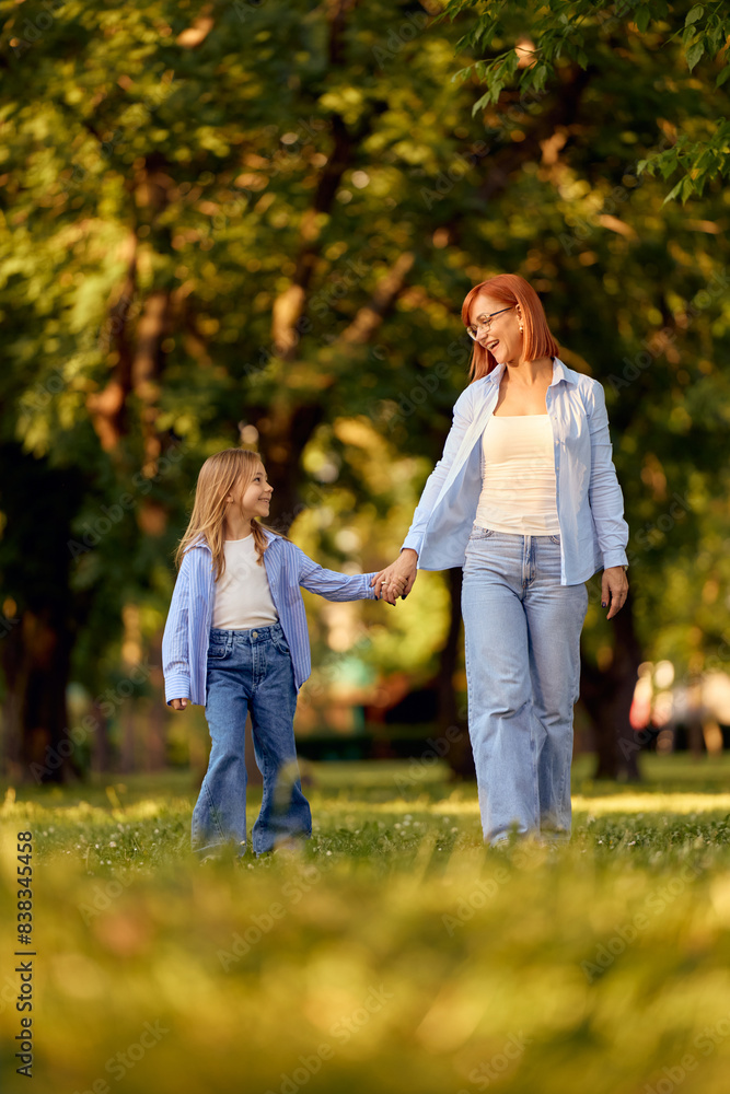 Mother and daughter with matching outfits walking through the park, holding hands, smiling. Mother and daughter with matching outfits walking through the park, holding hands, smiling.