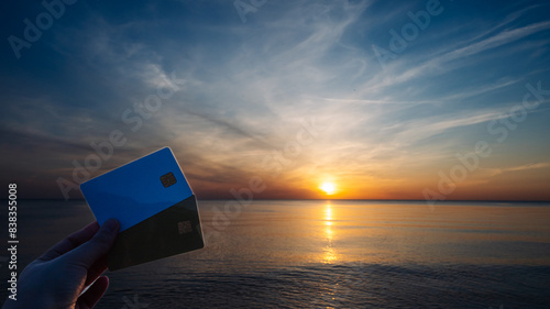 A person holding two credit cards in front of a beautiful sunset