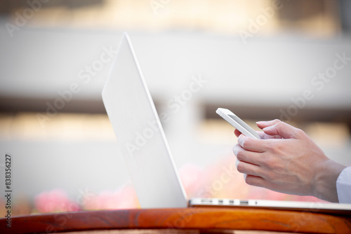 Closeup image of woman hands holding, using smart, mobile phone and laptop computer outdoors  photo
