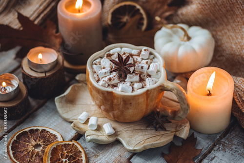 Spicy sweet fall hot drink: delicious pumpkin latte with cinnamon, marshmallow with salted caramel. Served in handmade artisan mug in shape of pumpkins, cozy home decor with candles, dry autumn leaves