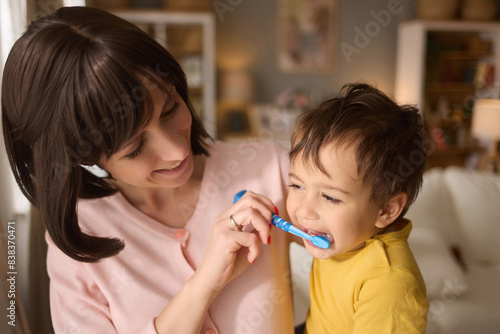 Mother teaching and helping her son brush his teeth at home