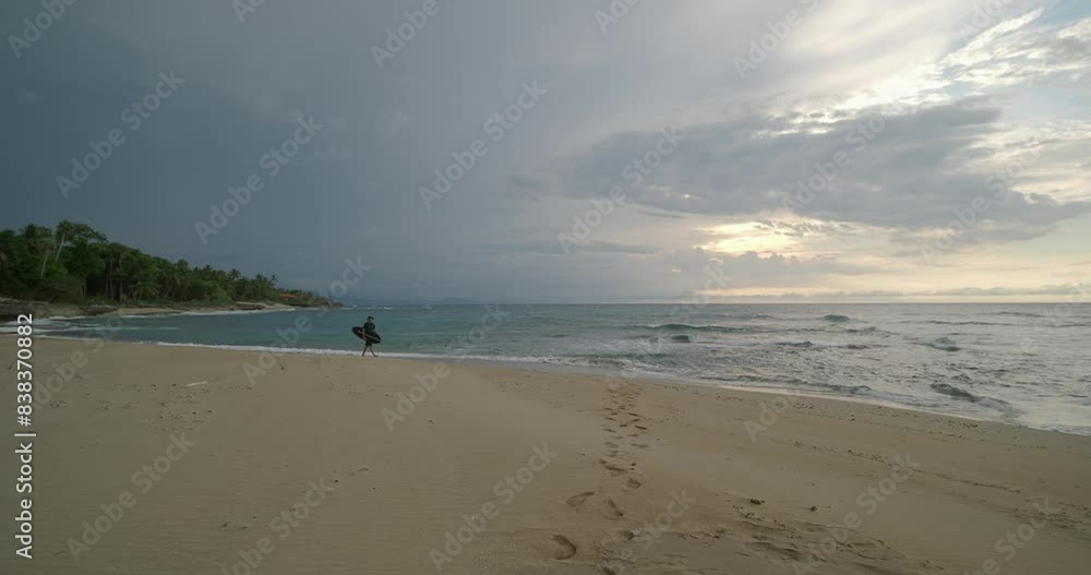 Surfer man walks on sandy beach with surfboard near ocean at rainy evening. Surfer man walks on sandy beach with surfboard near ocean at rainy evening.