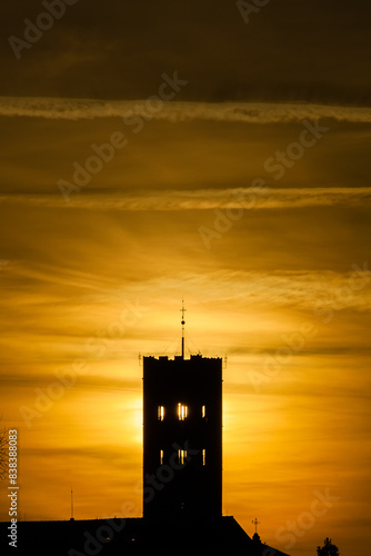 Lucca old skyline at sunset with cathedral bell tower silhouette and golden clouds