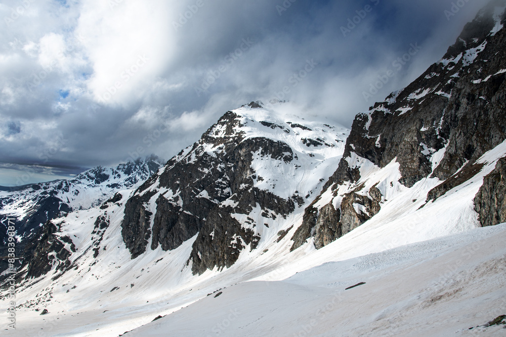 Play of light and shadow on a snowy mountain landscape with a mountain range dominated by a cloudy sky. Italy.