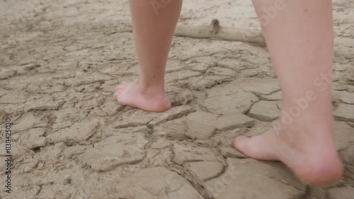 Man's feet are barefoot walking on dry cracked ground in drought. Concept of global warming of climate on earth.