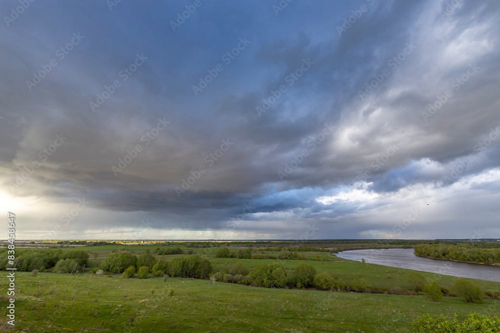 A serene meadow overlooks a winding river under a dramatic sky filled with storm clouds and patches of blue, capturing the beauty of nature's ever-changing weather patterns A serene meadow overlooks a winding river under a dramatic sky filled with storm clouds and patches of blue, capturing the beauty of nature's ever-changing weather patterns