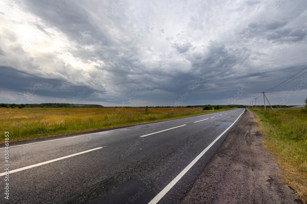 A paved road stretches out through a field, with a vast, gray sky overhead. The air is filled with the anticipation of a storm. A paved road stretches out through a field, with a vast, gray sky overhead. The air is filled with the anticipation of a storm.