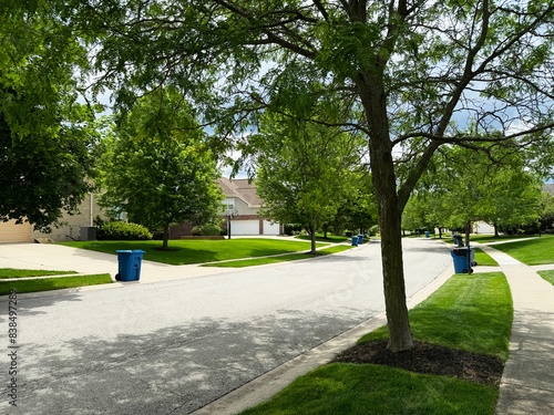 Blue trash cans line the street on trash day in an Indiana Neighborhood with a trash truck in the background with copy space.