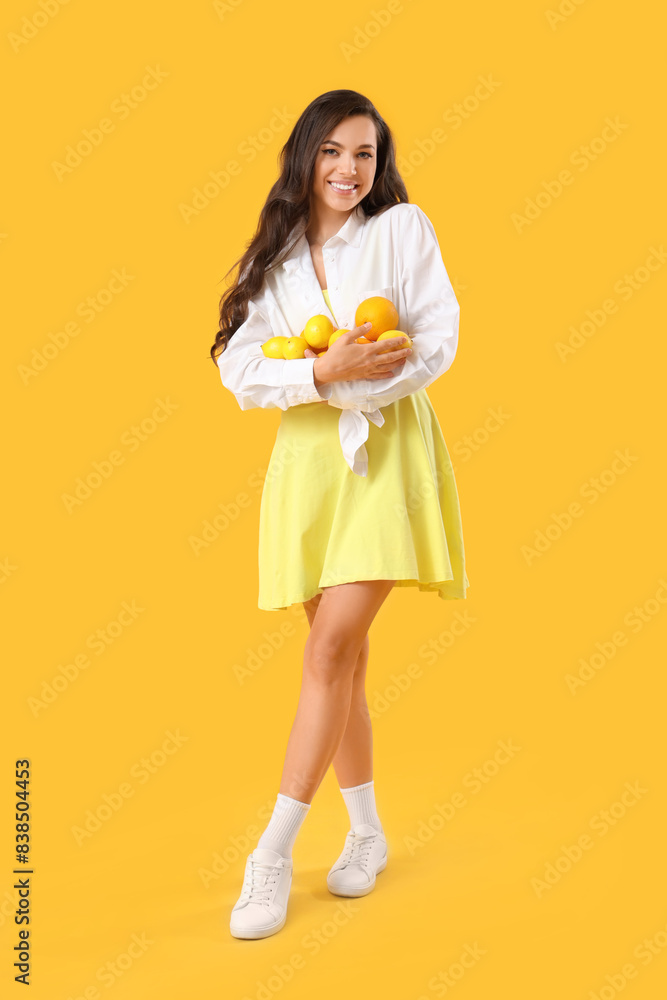 Pretty young woman holding many lemons on yellow background Pretty young woman holding many lemons on yellow background