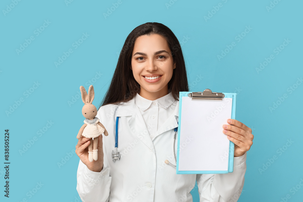 Portrait of female doctor with plush toy and clipboard on blue background Portrait of female doctor with plush toy and clipboard on blue background