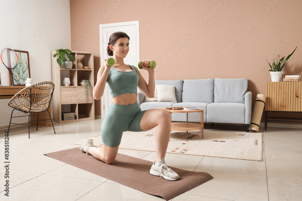 Obraz premium Sporty young woman training with dumbbells on mat at home