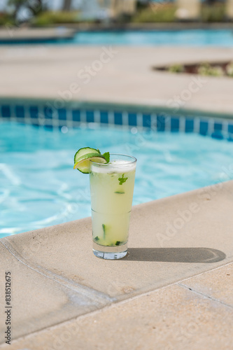 Vertical color photo of a mint mojito sitting on the side of a blue pool- summer resort vacation