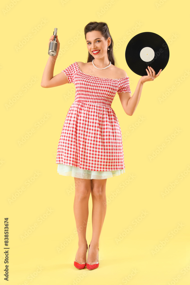 Portrait of beautiful pin-up woman with microphone and vinyl disk on yellow background Portrait of beautiful pin-up woman with microphone and vinyl disk on yellow background
