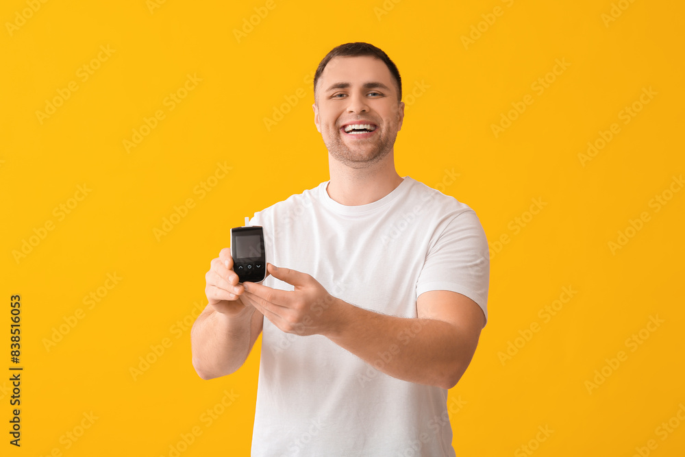 Handsome young happy diabetic man with glucometer on yellow background Handsome young happy diabetic man with glucometer on yellow background