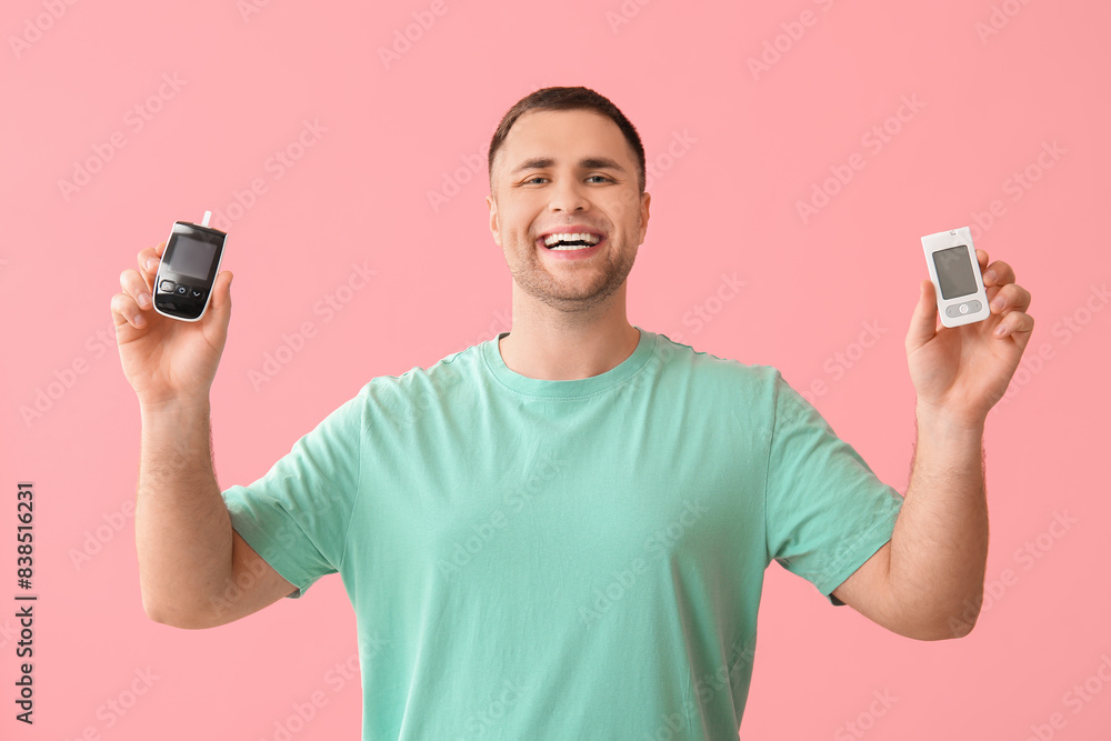 Handsome young happy diabetic man with glucometers on pink background Handsome young happy diabetic man with glucometers on pink background