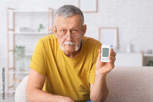 Senior man with glucometer sitting on sofa at home. Diabetes concept