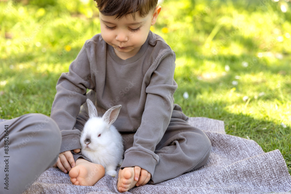 cute kid playing with rabbit outside in park or garden, hugging.child with bunny ears on head sitting on picnic blanket.animal in basket, blossom tree in background.spring easter time. cute kid playing with rabbit outside in park or garden, hugging.child with bunny ears on head sitting on picnic blanket.animal in basket, blossom tree in background.spring easter time.