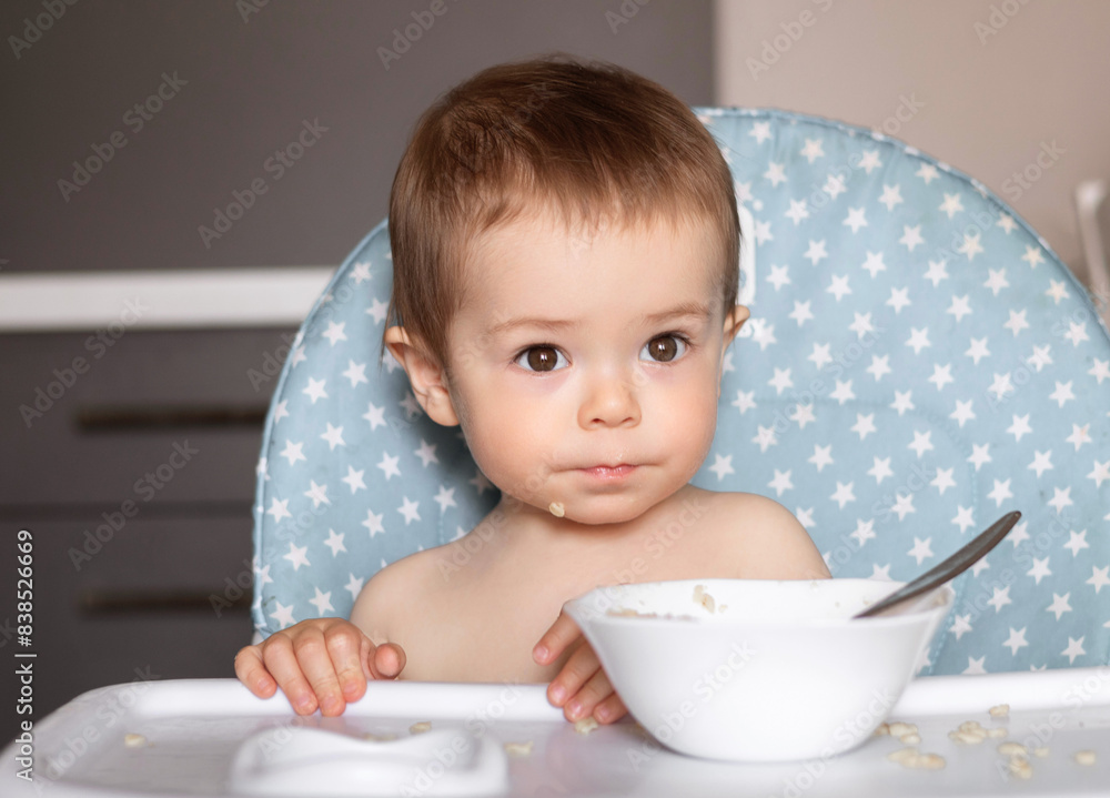 adorable baby boy toddler in highchair eating porridge, crying and feeling dissatisfied.kid child making whims, air and graces,refuse to eat healthy breakfast.plate on floor,dirt on table. adorable baby boy toddler in highchair eating porridge, crying and feeling dissatisfied.kid child making whims, air and graces,refuse to eat healthy breakfast.plate on floor,dirt on table.